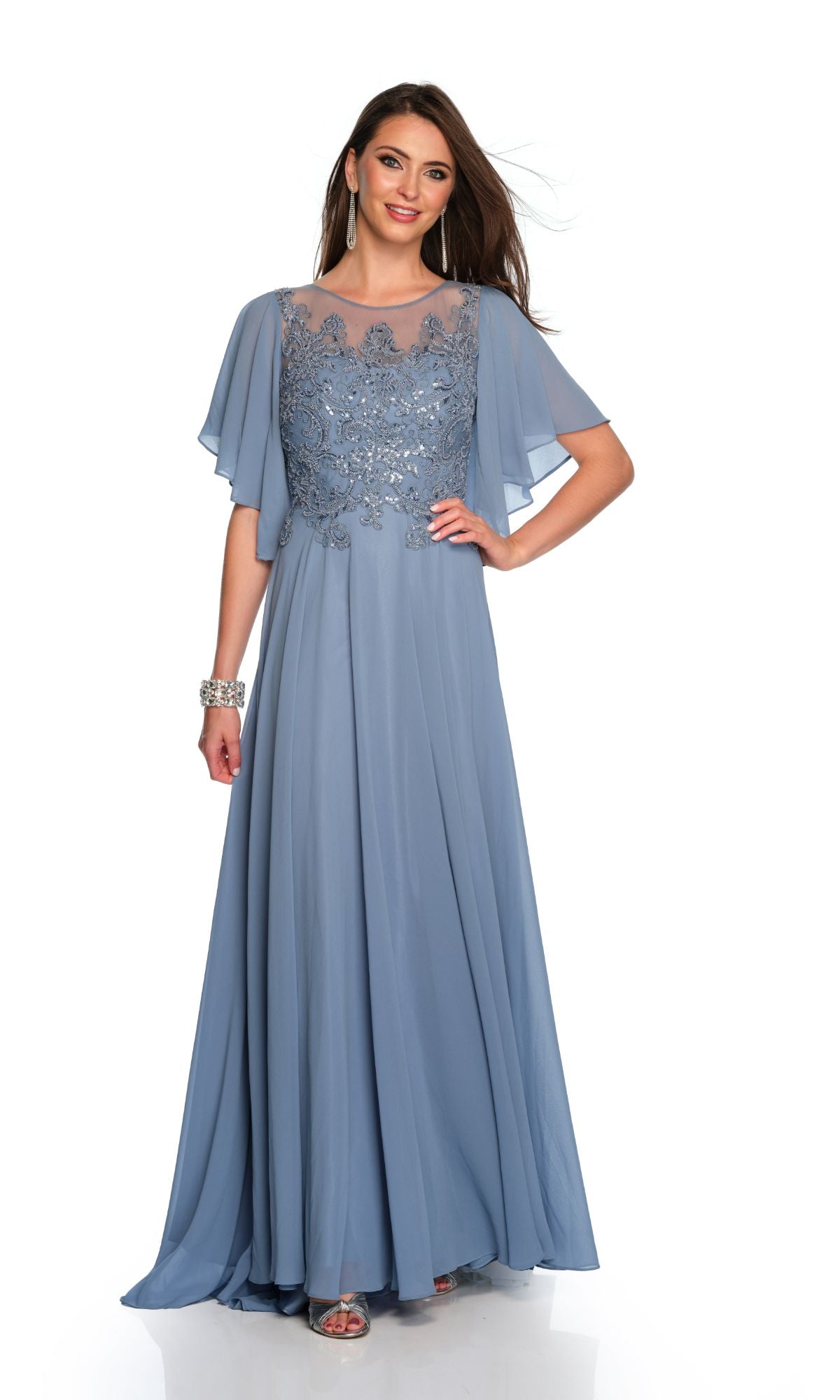 A woman wears the Dave & Johnny Long Prom Dress 11676, a floor-length light blue gown with lace bodice detailing and sheer flutter sleeves, paired with earrings and a bracelet.